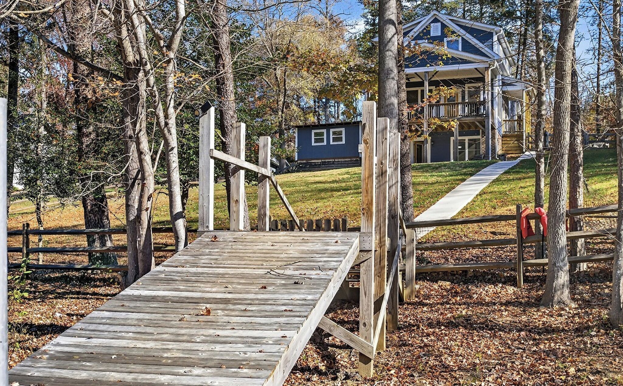 A wooden deck leading to a house with a porch, surrounded by trees and a grassy area.