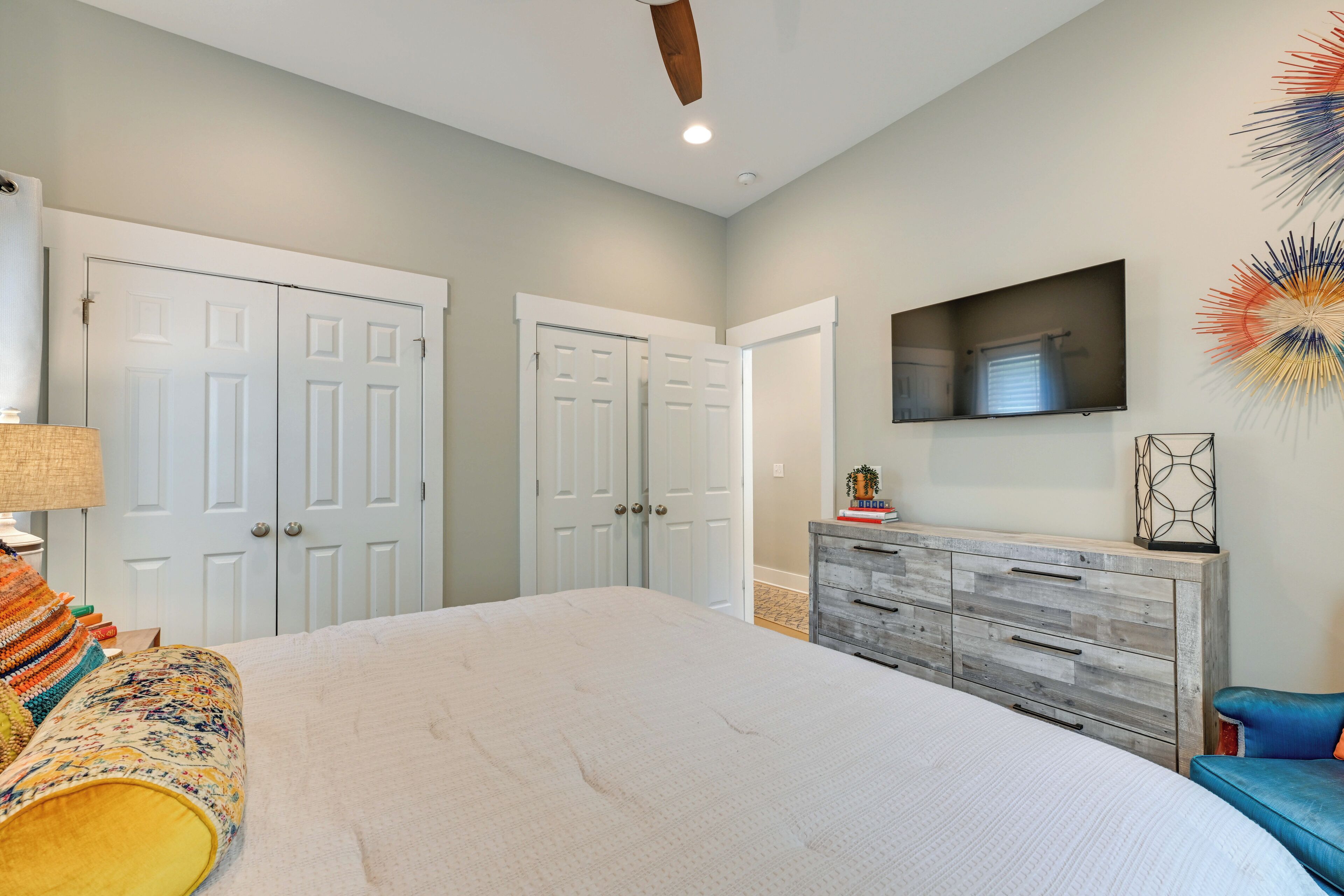 A bedroom with a bed, a dresser, a TV, and two doors.