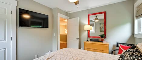 Une chambre à coucher comprenant un lit, un ventilateur de plafond, une commode, un miroir et une porte donnant sur une autre pièce.