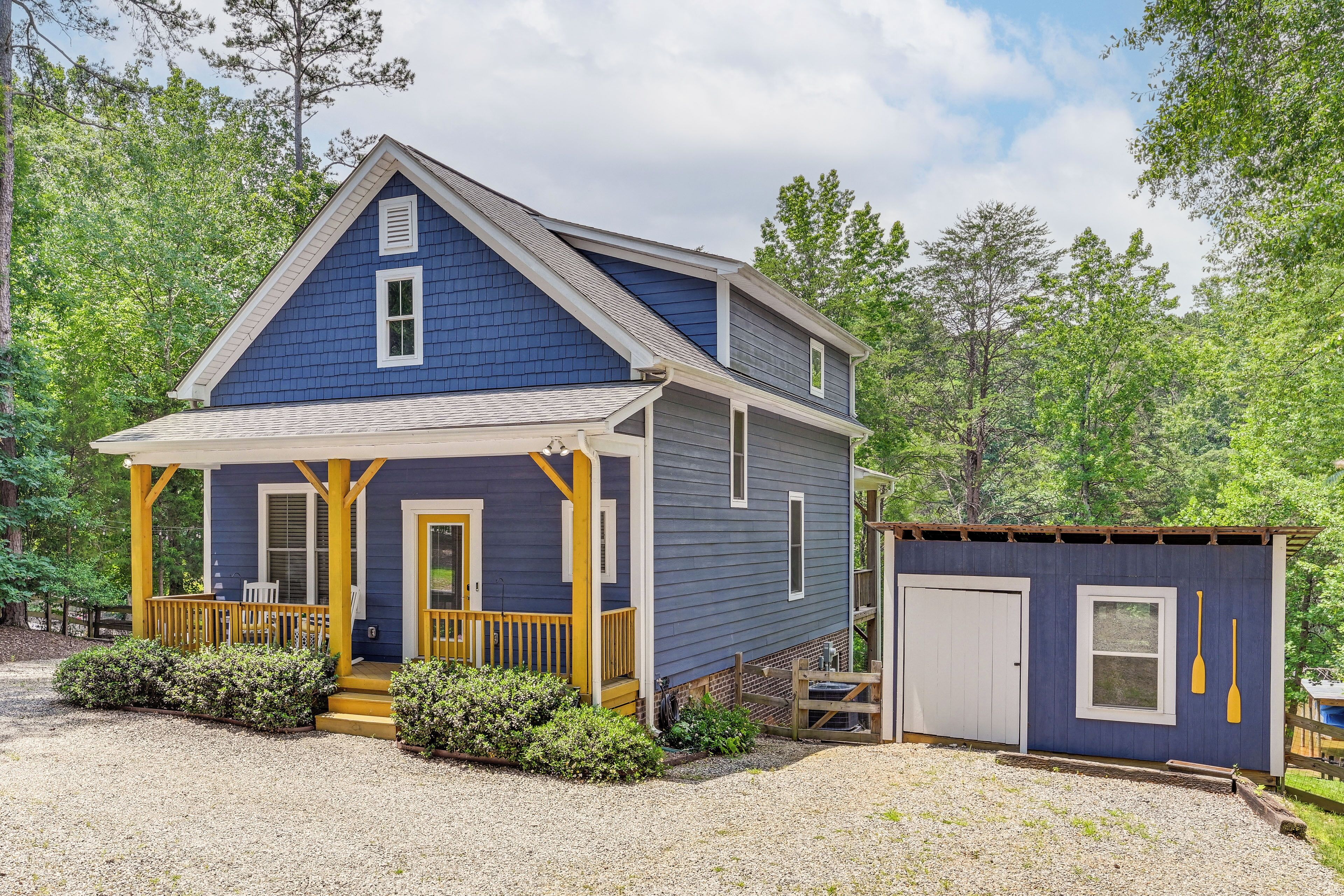 A two-story house with a porch, a small shed, and a gravel driveway.