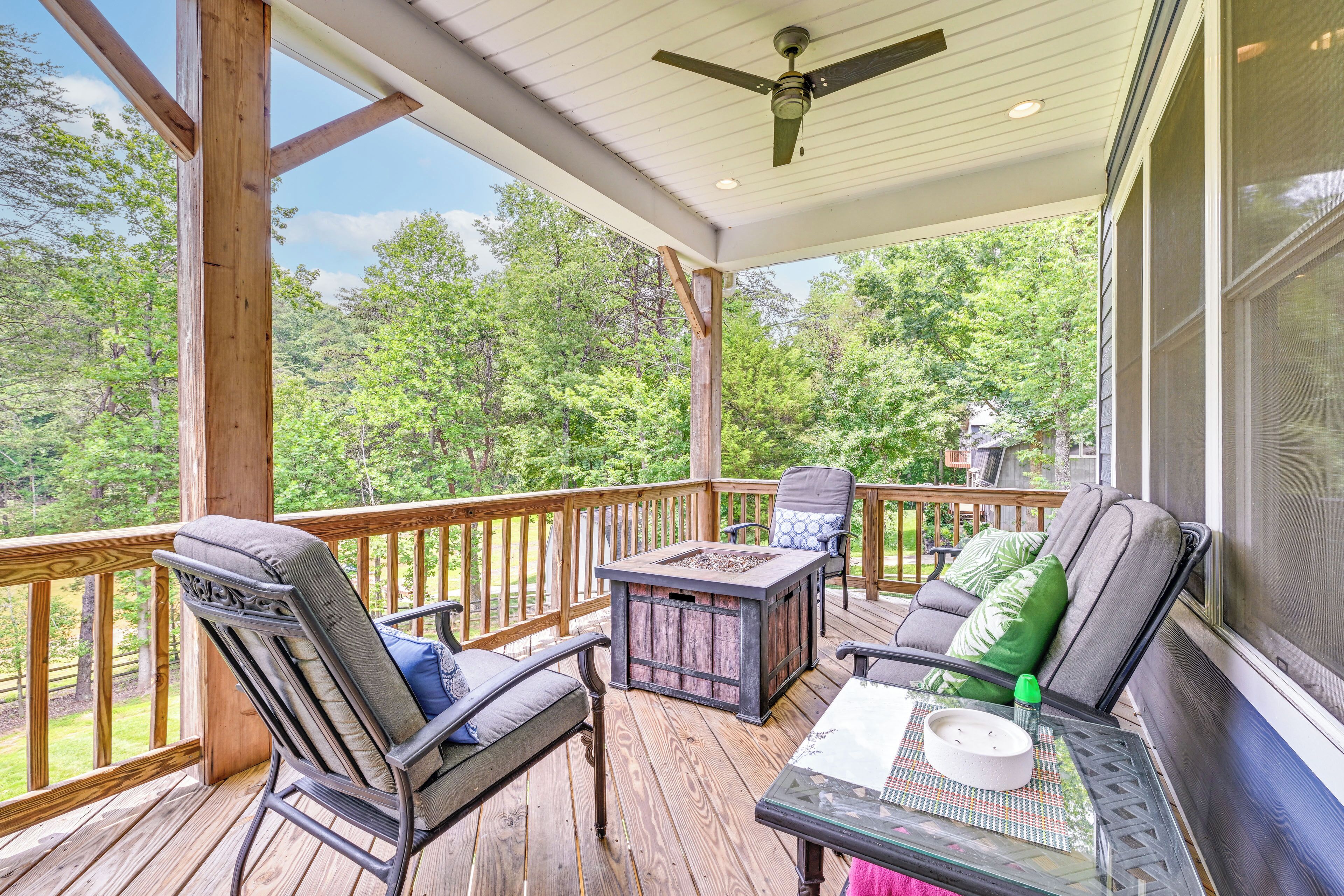 A covered outdoor deck with wooden railings, a ceiling fan, and seating with cushions.