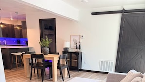 Una sala de estar moderna con un sofá modular, un comedor con sillas y una mesa, y una cocina al fondo.