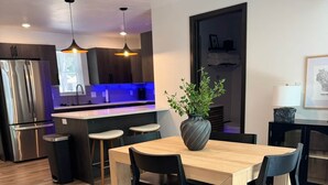 Una cocina moderna con una isla central, sillas negras y una mesa de comedor de madera.