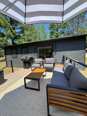 Eine moderne Terrassenanlage im Freien mit Holzdeck, einer schwarzen Couch, einem Holztisch und Grillplatz.