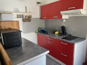 Eine kleine Küche mit roten und weißen Schränken, einer eingebauten Mikrowelle, einer Kaffeemaschine und einem kleinen Spülbecken.