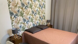A neatly made bed with a pink bedspread, two bedside lamps, a white chair, and a wall with a tropical leaf pattern. - Self-contained apartment in the heart of the garrigues. Spa garden. pets allowed (Pignan)