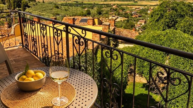 Un balcone con un tavolo, una ciotola di limoni e un bicchiere di vino bianco.