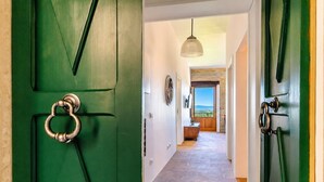 Un corridoio con porte verdi, un lampadario e vista su un balcone.