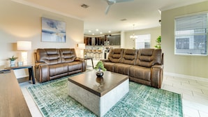 A living room with two brown leather sofas, a coffee table, a ceiling fan, and a kitchen in the background. - Disney! Universal! Free On-site Resort For All! (Kissimmee)