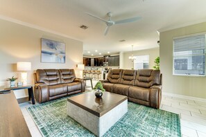 A living room with two brown leather sofas, a coffee table, a ceiling fan, and a kitchen in the background. - Disney! Universal! Free On-site Resort For All! (Kissimmee)