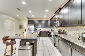 A modern kitchen with dark cabinets, granite countertops, stainless steel appliances, and a bar area. - Disney! Universal! Free On-site Resort For All! (Kissimmee)
