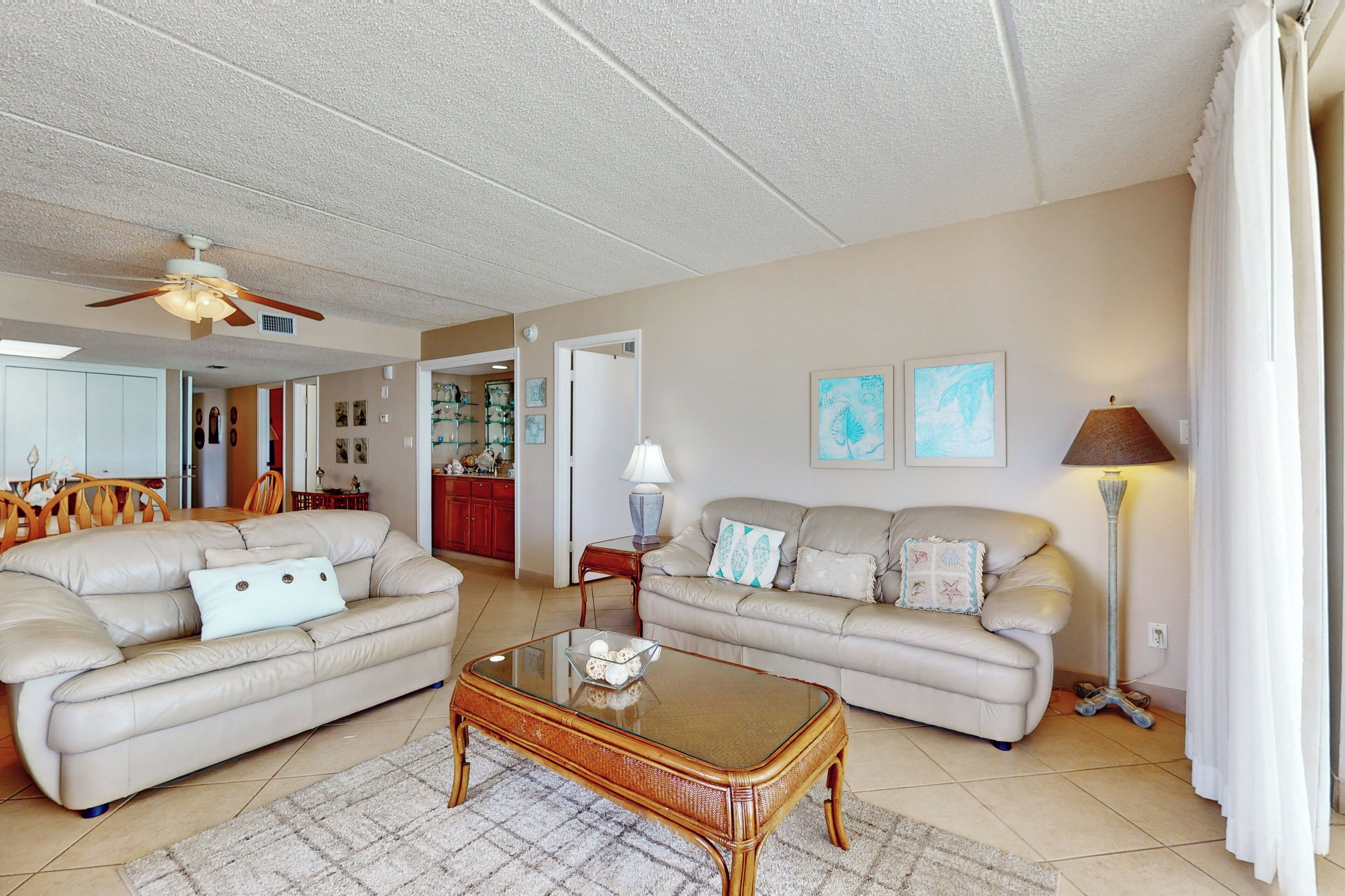A living room with two beige sofas, a glass coffee table, a ceiling fan, and a floor lamp.