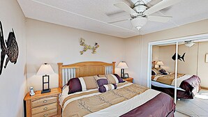 Une chambre à coucher comprenant un lit, des tables de chevet, un ventilateur de plafond, des œuvres d’art murales et un miroir.