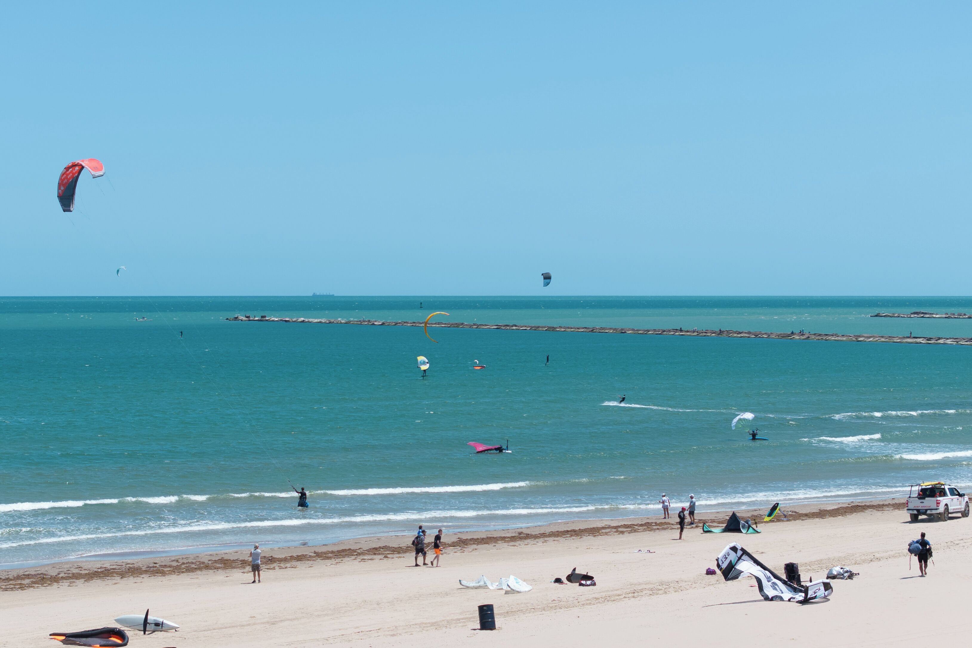 Een strand met mensen, een pier en een heldere lucht.