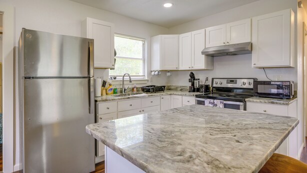 A kitchen with white cabinets, a stainless steel refrigerator, a microwave, and a stove.