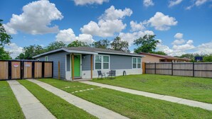 A single-story house with a green door, a small front yard with a concrete path, and a fenced backyard.