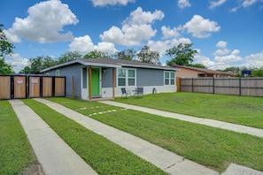 A single-story house with a green door, a small front yard with a concrete path, and a fenced backyard. - 7 Mi to Dtwn Satx! Bright Home w/ Yard & Grill (San Antonio)