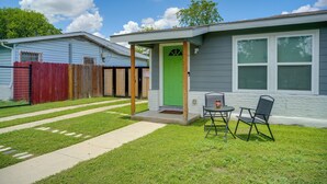 A single-story house with a green door, a small porch with two chairs, and a fenced backyard.