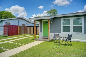A single-story house with a green door, a small porch with two chairs, and a fenced backyard. - 7 Mi to Dtwn Satx! Bright Home w/ Yard & Grill (San Antonio)