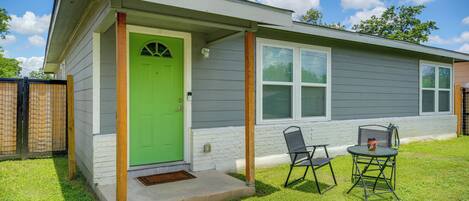 A single-story house with a green door, a covered porch, and two chairs outside.