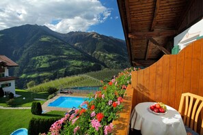 Un balcon avec une piscine, des fleurs et une table garnie de fruits.