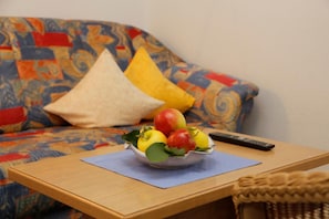 Ein Sofa mit bunten Kissen, einer Fernbedienung und einer Obstschale auf einem Holztisch.
