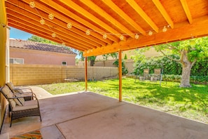 A covered patio with a concrete floor, a wicker chair, and a string of lights.