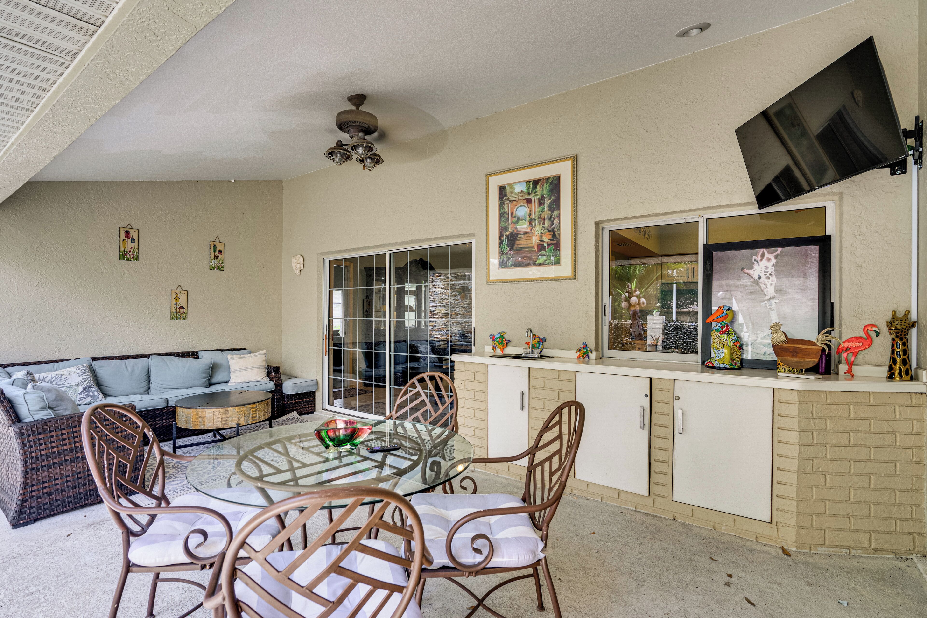 A dining area with a glass table, wicker chairs, a sofa, and a kitchen counter with decorative items.