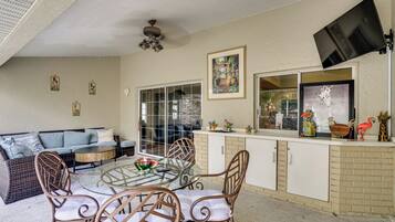 A dining area with a glass table, wicker chairs, a sofa, and a kitchen counter with decorative items.