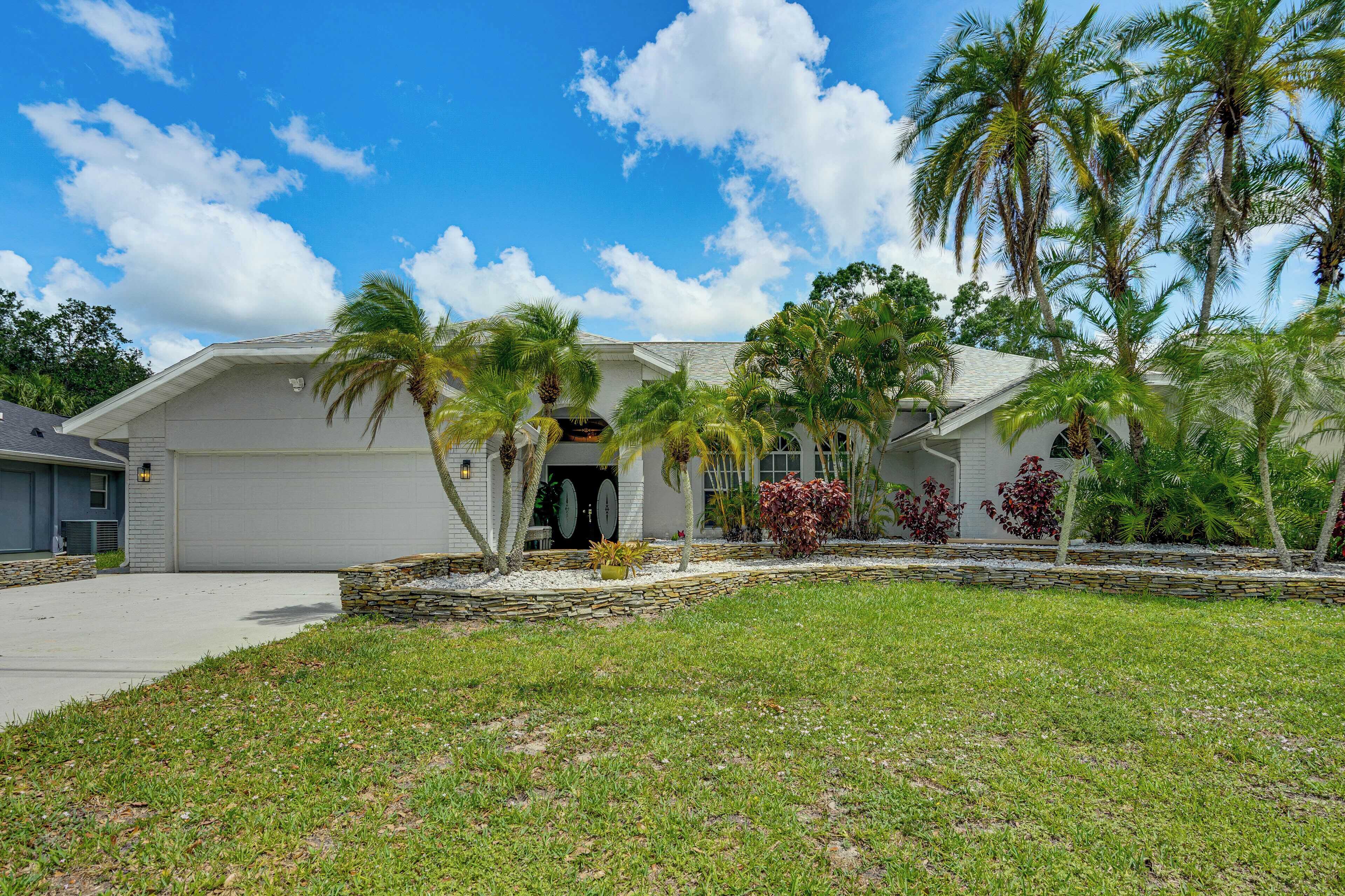 A two-story house with a garage, surrounded by a well-maintained lawn and palm trees.