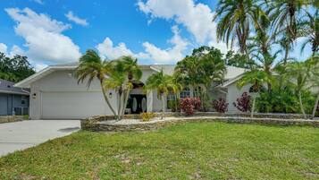 A two-story house with a garage, surrounded by a well-maintained lawn and palm trees.