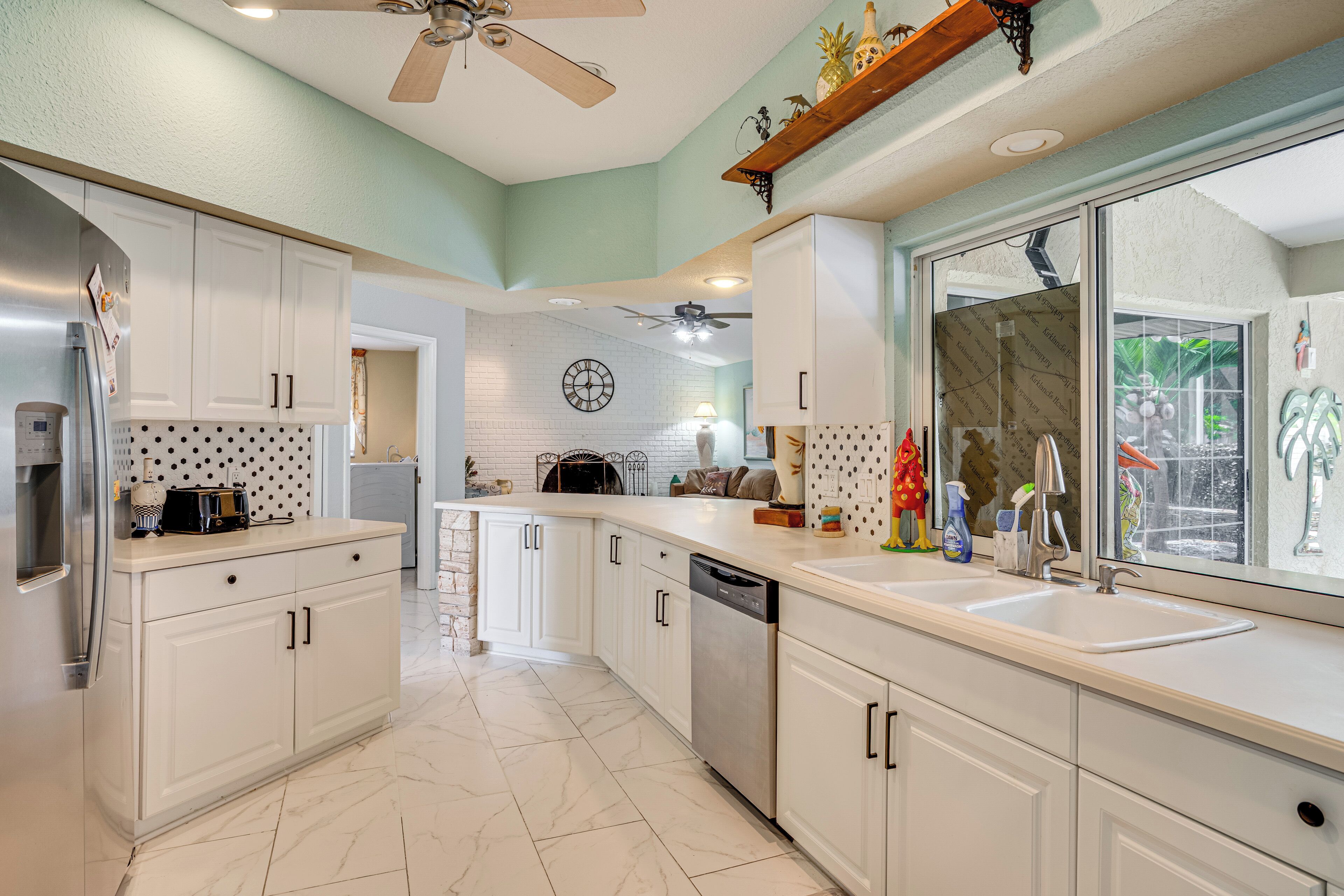 A kitchen with white cabinets, a dishwasher, a large window, and a ceiling fan.