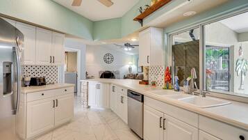 A kitchen with white cabinets, a dishwasher, a large window, and a ceiling fan.