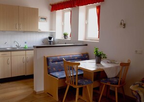 Eine Küche mit Holzausstattung, einer Spüle, einem Fenster mit roten Vorhängen, einer Bank und einem Tisch mit Stühlen.
