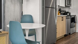 Une cuisine moderne équipée d’un réfrigérateur en acier inoxydable, d’un four à micro-ondes et d’un coin repas avec une table blanche et des chaises de couleur turquoise.