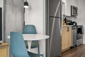 A modern kitchen with a stainless steel refrigerator, a microwave, and a dining area with a white table and teal chairs. - Boulevard Stays Modern Highrise Studio Sky Pool & Gym (Phoenix)