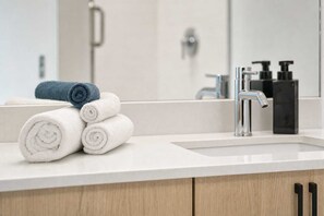 A bathroom with a white sink, a mirror, and a towel rack with rolled towels. - Boulevard Stays Modern Highrise Studio Sky Pool & Gym (Phoenix)