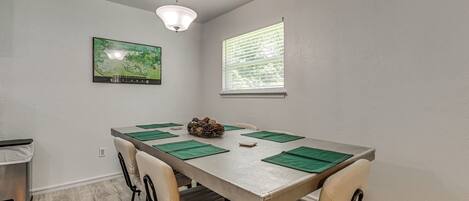 A dining area with a table, chairs, a ceiling light, a window, and a framed picture on the wall.