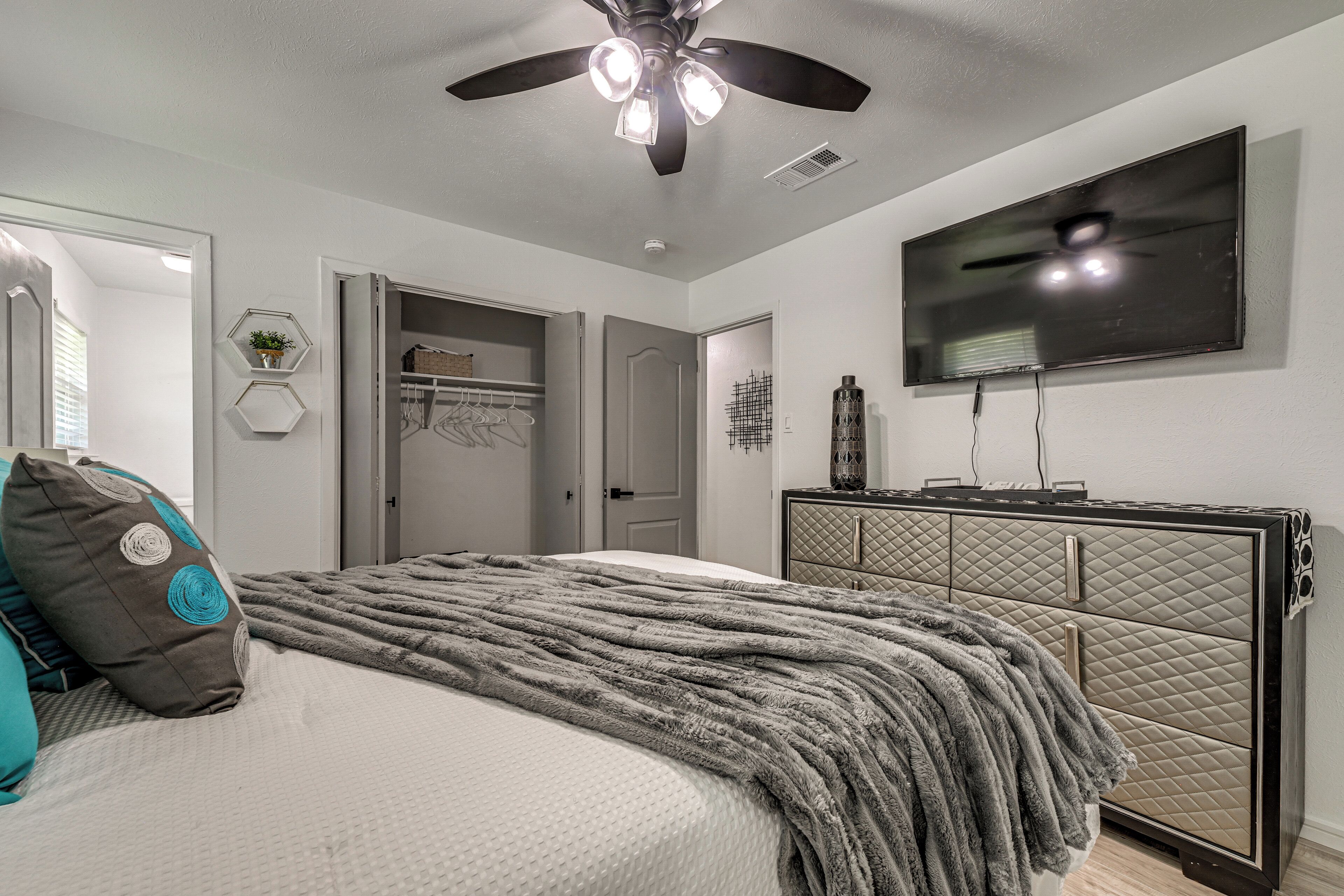 Quarto com cama, ventoinha no teto, televisão, cômoda e armário.
