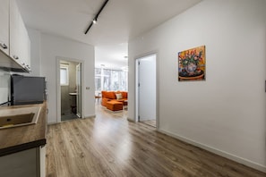 Eine moderne Küche mit Einbauofen und Spüle, ein Flur, der in einen Wohnbereich mit Sofa führt, und ein Gemälde an der Wand.