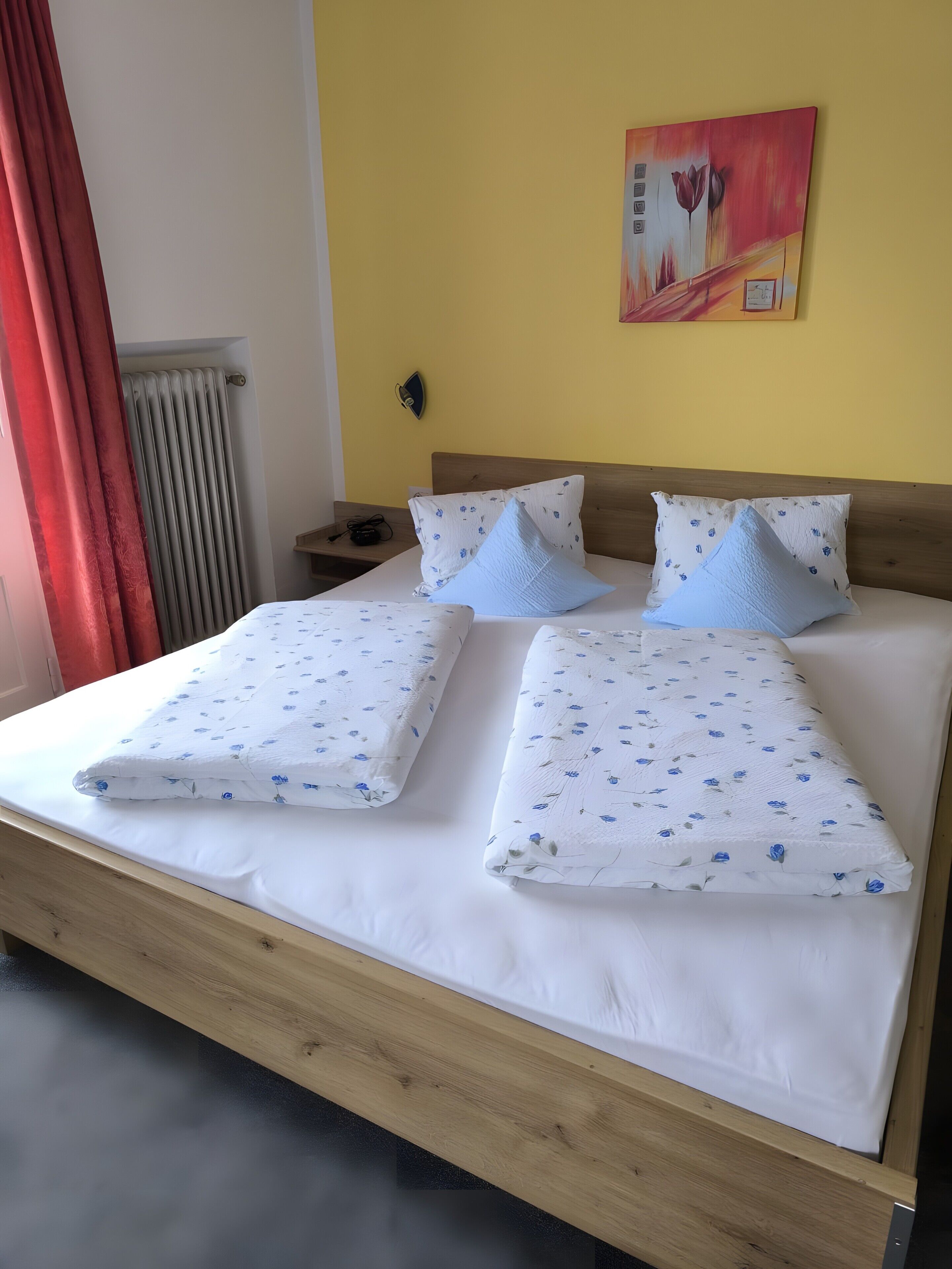 A bed with white bedding and blue floral patterns, a wooden headboard, and a wall clock.
