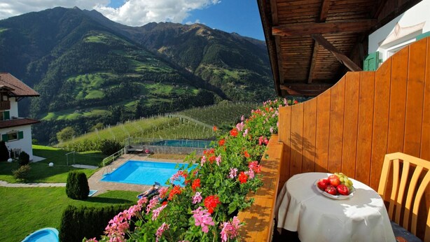 Un balcon avec une piscine, des fleurs et une table garnie de fruits.