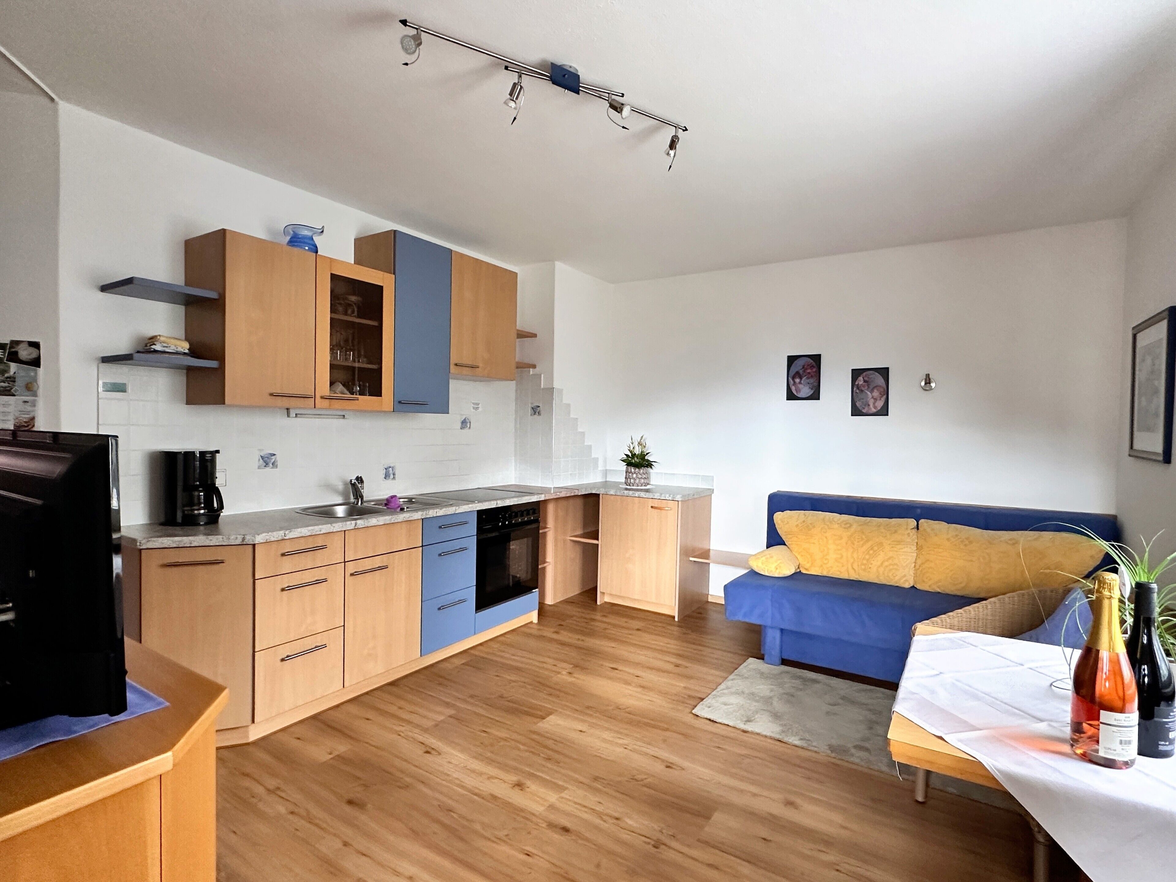 A modern kitchen with wooden cabinets, a built-in dishwasher, and a dining area with a blue sofa and a table.