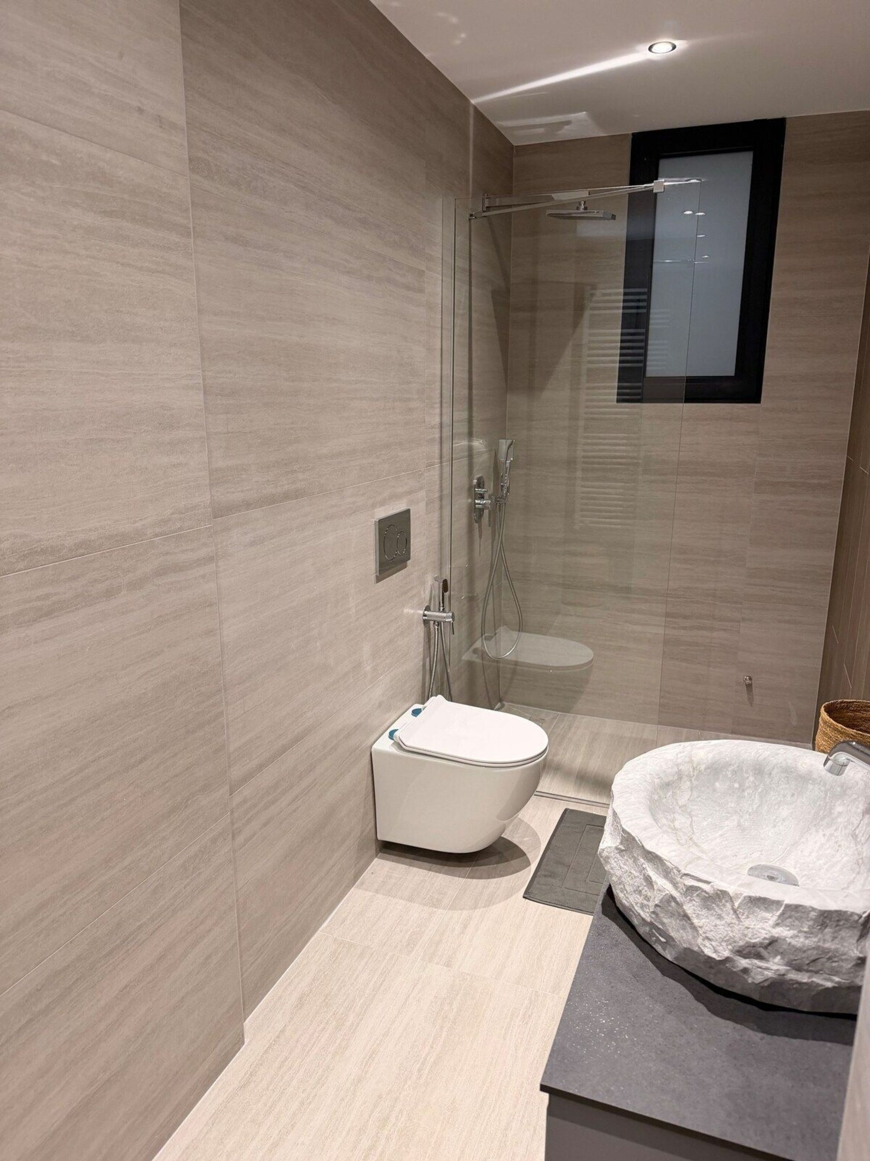 A modern bathroom with a glass-enclosed shower, a white toilet, and a stone sink.