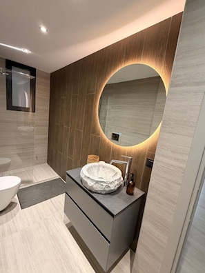 A modern bathroom with a round mirror, a white sink, and a wooden vanity. - Elliniko Elite Residence (Elliniko)