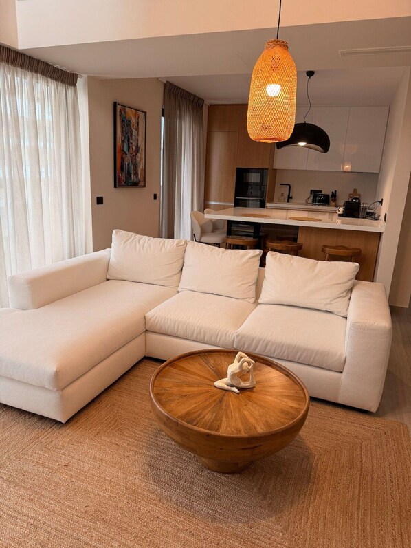 Un salon moderne avec un canapé d’angle, une table basse en bois et un luminaire suspendu.