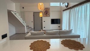 Una sala de estar moderna con una escalera, un sofá, un televisor de pantalla plana y un amplio ventanal con cortinas.