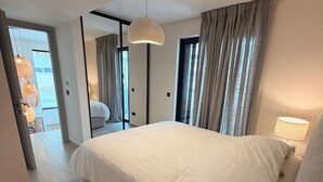 Una habitación de hotel moderna con una cama grande, una mesita de noche, una lámpara y vistas a la ciudad a través de la ventana.