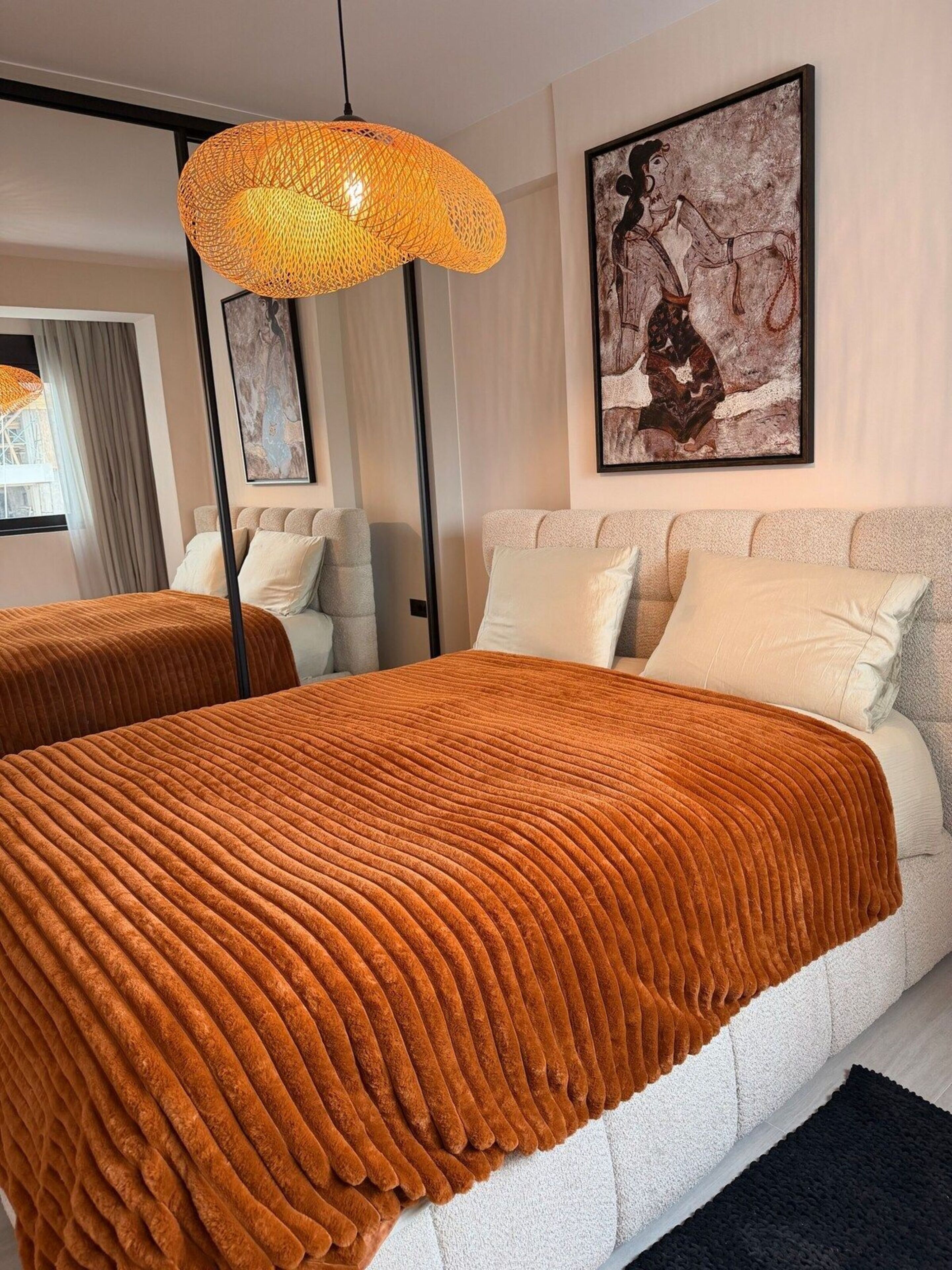 A modern bedroom with a large bed, a hanging orange light fixture, and a framed abstract painting on the wall.