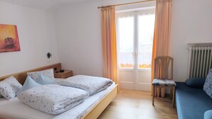 Een slaapkamer met twee bedden, een stoel, een bank, een nachtkastje en een raam met gordijnen.